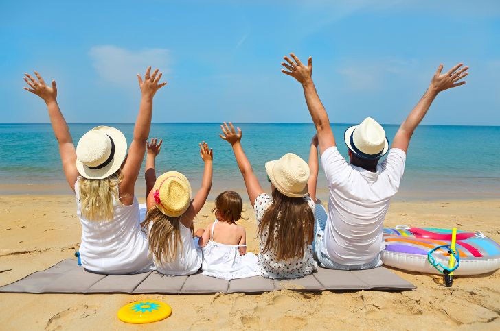 Family sitting on the beach with their arms up having fun